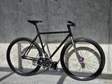 TrackloX Midnight Mirage TLX20MM – a stylish black single-speed fixie bike with a chrome fork and purple hubs, built for urban riding, bikepacking, and tracklocross