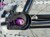 Close-up of TrackloX Midnight Mirage TLX20MM rear dropout, featuring an XFIXXI-branded horizontal dropout, purple anodized axle bolts, and a KMC Rust Buster chain. Designed for secure and precise wheel alignment