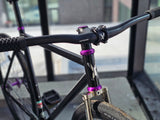 Close-up of TrackloX Midnight Mirage TLX20MM handlebars, stem, and head tube. Features black riser bars, purple anodized accents, and a chrome fork. Designed for urban riding, bikepacking, and tracklocross