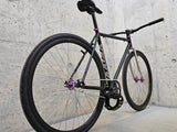 TrackloX Midnight Mirage TLX20MM – a sleek black single-speed fixie bike with a chrome fork, purple hubs, and Arisun tires, captured from a rear-angle perspective. Built for urban riding, bikepacking, and tracklocross