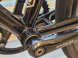 Close-up of the XFIXXI TrackloX Urban Bike's bottom bracket and crankset. Featuring a black aluminum crank arm with the 'XFIXXI' logo, a sealed bearing bottom bracket, and a durable chromoly frame