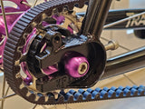 Close-up of the XFIXXI TrackloX Urban Bike's rear dropout and Gates CDX Carbon Belt Drive system. Featuring a black aluminum rear dropout with the 'XFIXXI' logo, a purple anodized axle bolt, and a high-flange sealed bearing hub for secure and smooth performance