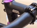 Close-up of the XFIXXI TrackloX Urban Bike's handlebar and stem. Featuring a black aluminum stem with the 'XFIXXI' logo, secured with hex bolts, and paired with a riser handlebar for urban riding control